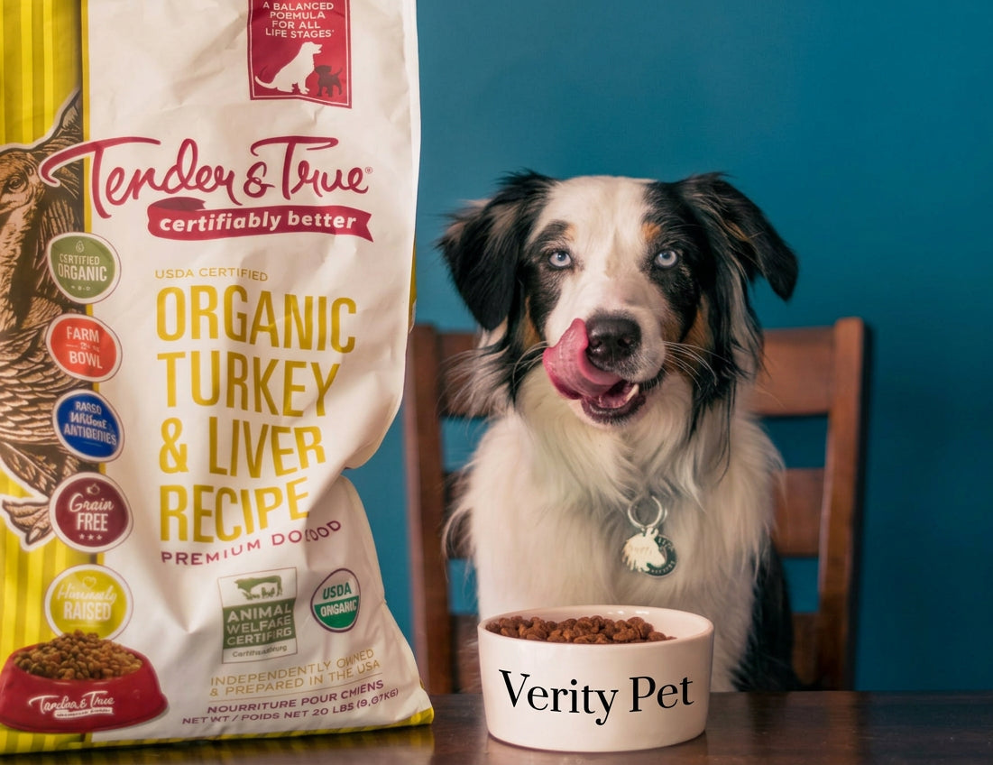 Dog beside Tender & True Organic Turkey & Liver dry dog food bag and assorted Tender & True canned dog foods