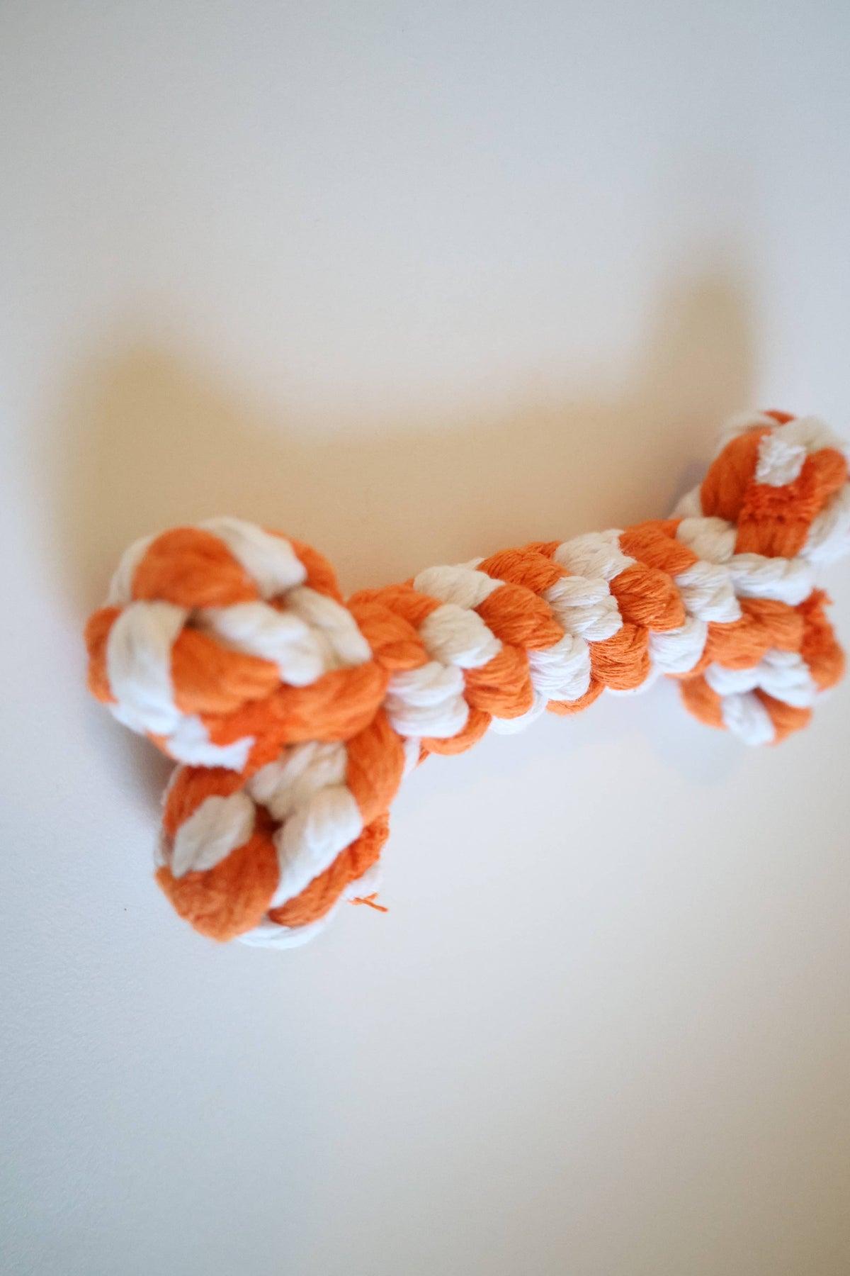 Side view of a handmade orange and white rope bone dog toy