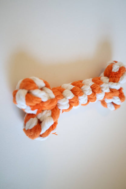 Side view of a handmade orange and white rope bone dog toy